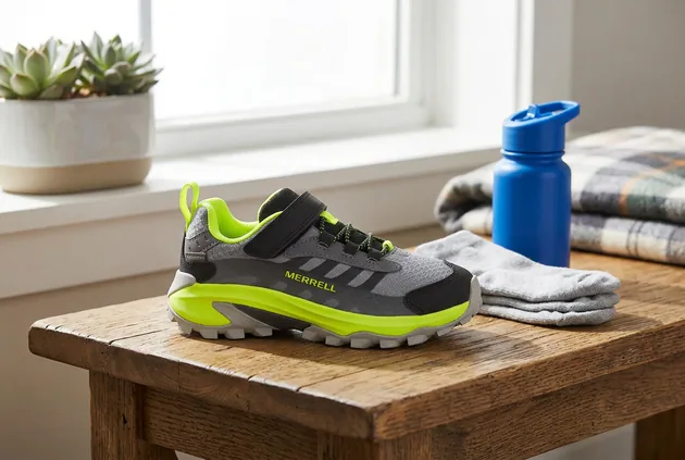 Merrell Moab Speed 2 Low waterproof kids hiking shoe on a wooden table beside folded socks, a water bottle, and a plaid blanket